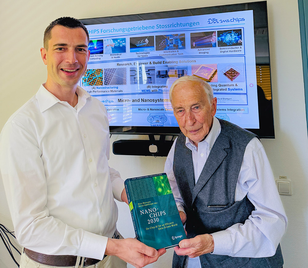 The picture shows Niels Quack, the current director of IMS CHIPS, on the left, and Bernd Hoefflinger, the first director at the IMS, on the right. Mr. Hoefflinger presents his latest publication to Mr. Quack. A scientific presentation on future innovations can be seen in the background.
